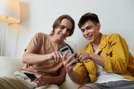 Téléchargez les photos : Joyeux jeunes hommes discutant de la nouvelle application mobile qu'ils téléchargent sur smartphone - en image libre de droit