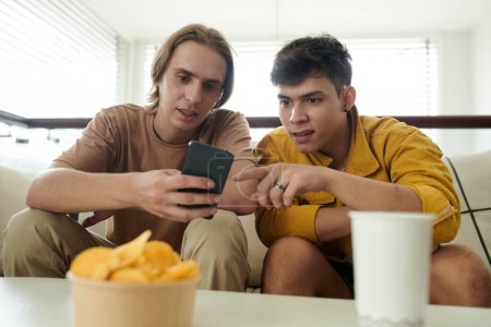 Téléchargez les photos : Les jeunes hommes discutent d'une nouvelle application sur smartphone - en image libre de droit