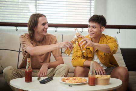 Téléchargez les photos : Joyeuses amies jetant des bouteilles de bière sur la table avec pizza et croustilles - en image libre de droit