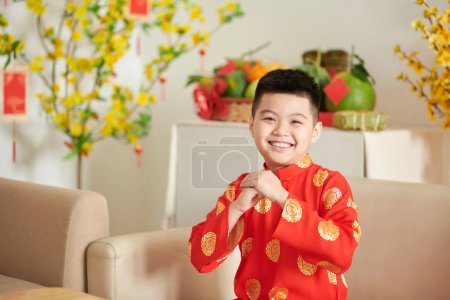 Téléchargez les photos : Petit garçon vietnamien souriant en robe ao dai faisant un geste de salutation - en image libre de droit
