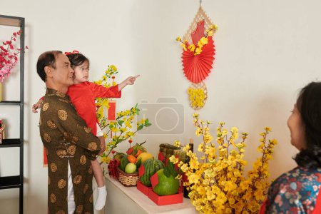 Foto de Abuelo mostrando niña Tet decoraciones que cuelga en las paredes del apartamento - Imagen libre de derechos