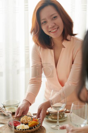 Foto de Mujer sonriente poniendo plato con verduras recogidas en la mesa de la cena - Imagen libre de derechos