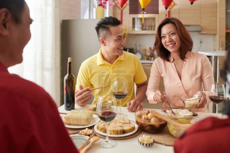 Téléchargez les photos : Couple asiatique souriant dégustant un dîner en famille et mangeant des plats traditionnels cuits pour la célébration du Têt - en image libre de droit