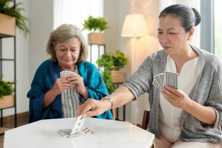 Senior women enjoying playing cards at round table in nursing home
