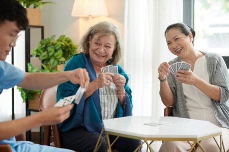 Joyful senior women looking at nursing home nurse choosing playing card