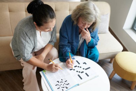 Photo for Pensive senior women solving crossword puzzle, view from above - Royalty Free Image
