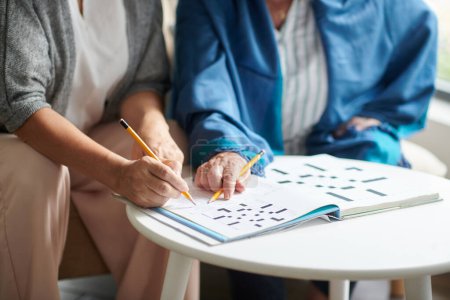 Photo for Cropped image of elderly women solving crossword puzzle together - Royalty Free Image