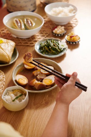 Téléchargez les photos : Mains de la personne qui mange du porc braisé et de la soupe aux œufs lors du dîner de vacances - en image libre de droit