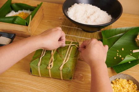 Photo for Hands tying wrapped Vietnamese square cake with bamboo strings - Royalty Free Image