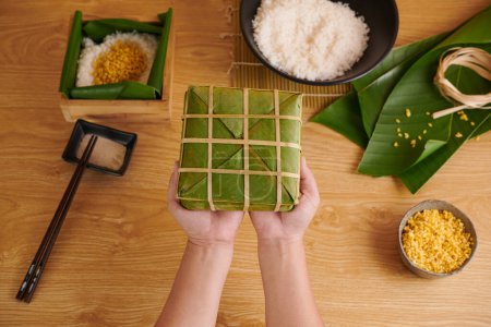 Photo for Hands holding wrapped traditional Vietnamese square cake prepared for Lunar New Year - Royalty Free Image