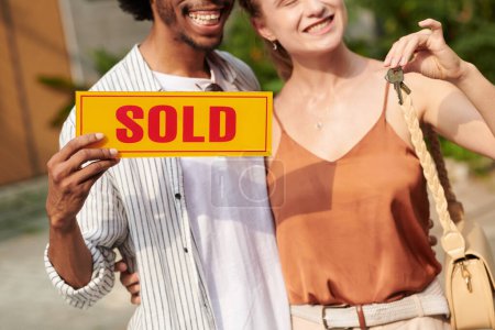 Téléchargez les photos : Image recadrée de couple heureux tenant signe vendu après l'achat de la maison - en image libre de droit
