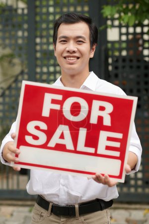 Foto de Retrato de agente de bienes raíces asiático feliz mostrando a la venta letrero - Imagen libre de derechos