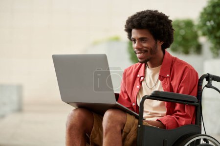 Foto de Sonriente hombre negro con discapacidad trabajando en el ordenador portátil - Imagen libre de derechos