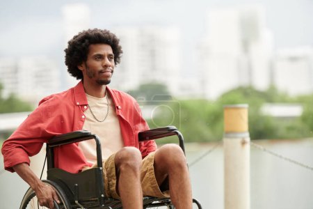 Téléchargez les photos : Portrait d'un homme noir souriant assis en fauteuil roulant et regardant ailleurs - en image libre de droit