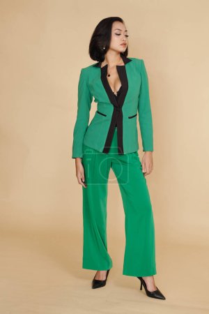 Photo for Asian fashion model demonstrating green elegant suit against beige background - Royalty Free Image