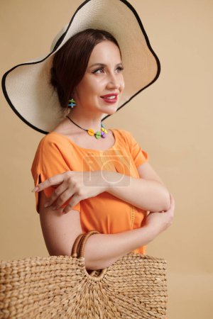 Photo for Young pretty woman in hat demonstrating accessories against orange background - Royalty Free Image