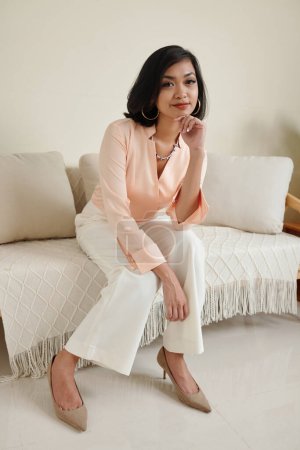 Téléchargez les photos : Portrait de jeune femme asiatique en costume élégant assis sur le canapé et regardant la caméra - en image libre de droit