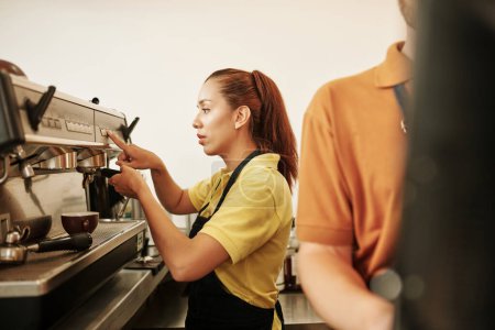 Foto de Nuevo botón del barista del coffeeshop en la máquina de café al hacer cappuccino para el cliente - Imagen libre de derechos