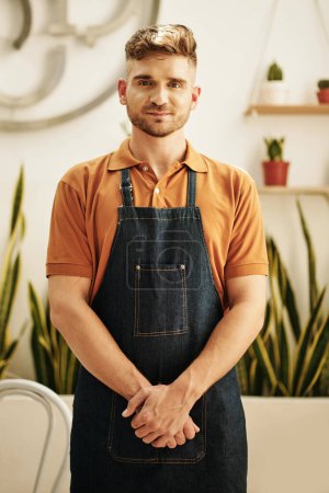 Photo for Portrait of positive coffeeshop barista in denim apron looking at camera - Royalty Free Image