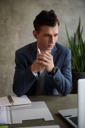 Téléchargez les photos : Jeune homme d'affaires en costume bleu foncé vérifier les rapports sur l'écran d'ordinateur portable - en image libre de droit