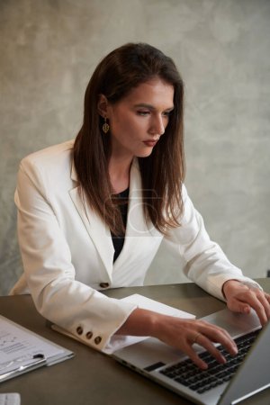 Téléchargez les photos : Portrait de jeune entrepreneur élégant travaillant sur ordinateur portable au bureau dans un bureau moderne - en image libre de droit