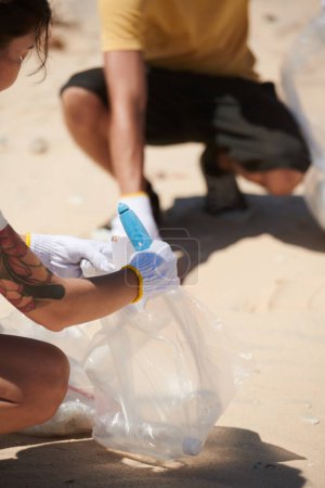 Téléchargez les photos : Image recadrée de personnes ramassant des ordures dans des sacs sur la plage de la mer - en image libre de droit