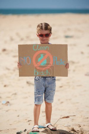 Téléchargez les photos : Petite fille souriante dans des lunettes de soleil montrant plage propre et pas de plaque en plastique - en image libre de droit