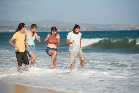Téléchargez les photos : Deux couples heureux sautant dans l'eau sur la plage de sable - en image libre de droit