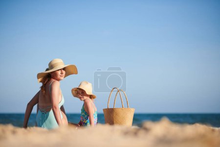 Photo for Mother and daughter in straw hats sunbathing on beach - Royalty Free Image