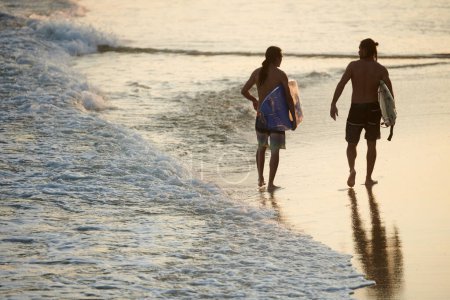Téléchargez les photos : Convient aux jeunes hommes marchant sur la plage de la mer après le surf - en image libre de droit