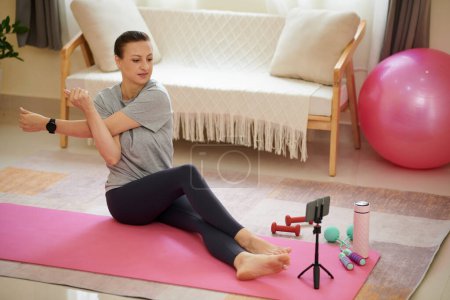 Foto de Mujer viendo video de entrenamiento en el teléfono inteligente y haciendo ejercicios de estiramiento - Imagen libre de derechos