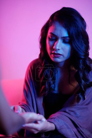 Photo for Serious woman looking closely at lines on palm to make predictions about career, love life, and happiness - Royalty Free Image