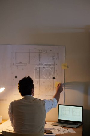 Téléchargez les photos : Architecte écrivant des idées sur des autocollants jaunes attachés au plan sur le mur au-dessus de son bureau - en image libre de droit