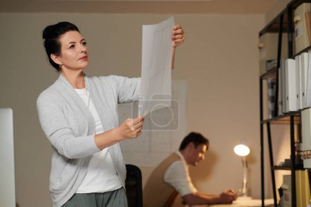 Photo for Portrait of pensive serious engineer looking at apartment florr plan in hands - Royalty Free Image