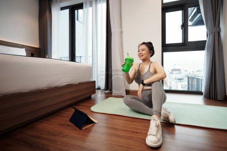 Téléchargez les photos : Joyeux jeune femme boire cocktail de protéines après l'exercice à la maison - en image libre de droit