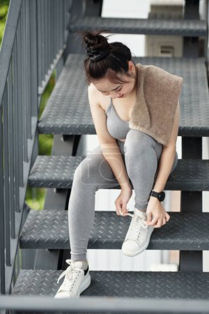 Téléchargez les photos : Sportswoman attacher lacets de chaussures lors de la lecture pour le jogging du matin - en image libre de droit