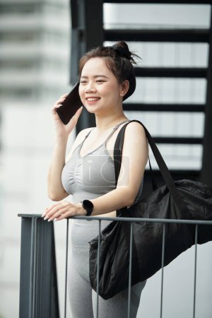 Téléchargez les photos : Jeune femme souriante avec sac de gym appelant au téléphone - en image libre de droit