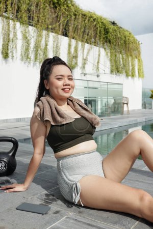 Téléchargez les photos : Joyeux jeune femme se reposant près de la piscine après avoir travaillé à l'extérieur - en image libre de droit