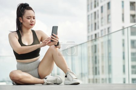 Téléchargez les photos : Sportswoman se reposer après l'entraînement et répondre aux messages dans son téléphone - en image libre de droit