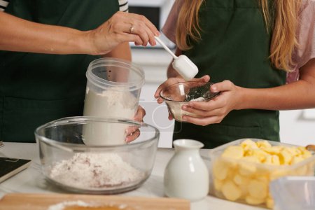 Photo for Closeup image of mother showing daughter how much flour she should put in bowl when making dough - Royalty Free Image