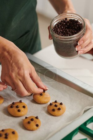 Foto de Imagen de primer plano de la mujer decorando galletas con chispas de chocolate - Imagen libre de derechos