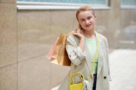 Photo for Portrait of smiling young woman with shopping bag standing on street - Royalty Free Image