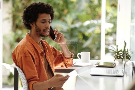 Téléchargez les photos : Jeune entrepreneur noir appelant le client pour discuter des détails de la commande - en image libre de droit