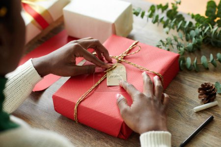 Téléchargez les photos : Mains de femme ajustant Merry étiquette de Noël sur cadeau enveloppé - en image libre de droit