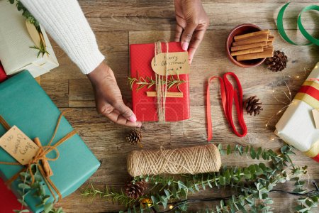 Téléchargez les photos : Mains de femme montrant petit cadeau de Noël enveloppé et décoré pour un membre de la famille - en image libre de droit