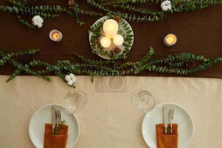 Photo for Christmas dinner table decorated with burning candles and eucalyptus branches, view from above - Royalty Free Image