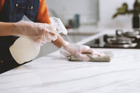 Téléchargez les photos : Image recadrée de la personne portant des gants lors du nettoyage du comptoir avec un désinfectant pulvérisé - en image libre de droit