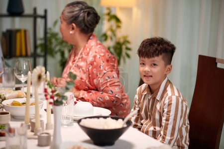 Photo for Little boy sitting at dinner table next to his grandmother - Royalty Free Image