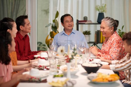 Téléchargez les photos : Heureuse famille vietnamienne parlant à la grande table du dîner lorsqu'elle est réunie pour célébrer les vacances - en image libre de droit