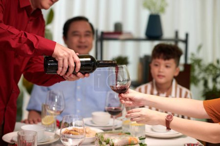 Téléchargez les photos : Les mains de l'homme versant du vin dans un verre de membre de la famille au dîner - en image libre de droit
